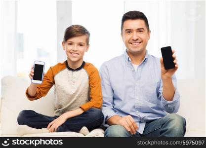 leisure, technology, technology, family and people concept - happy father and son showing smartphone blank screens at home