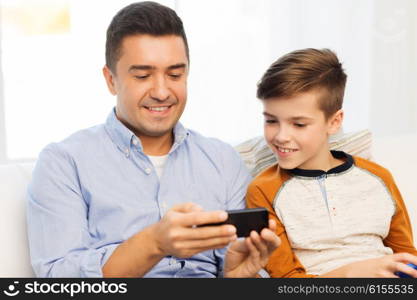 leisure, technology, technology, family and people concept - happy father and son with smartphone texting message or playing game at home