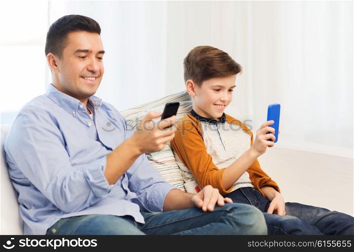 leisure, technology, technology, family and people concept - happy father and son with smartphones texting message or playing game at home