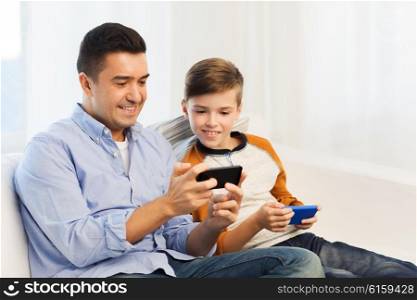 leisure, technology, technology, family and people concept - happy father and son with smartphones texting message or playing game at home