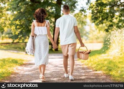leisure, vacation and people concept - happy couple with picnic basket and blanket walking at summer park. happy couple with picnic basket at summer park