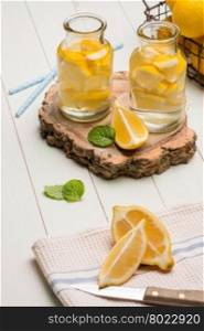 Lemon and lime slices in jars and straws in summer wooden background.