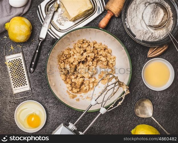 Lemon cookie or cake preparation with cooking ingredients. Butter and sugar mixing with hand mixer on dark kitchen table background , top view