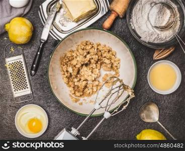 Lemon cookie or cake preparation with cooking ingredients. Butter and sugar mixing with hand mixer on dark kitchen table background , top view