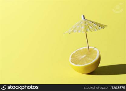 Lemon fruit and a cocktail umbrella stuck in it, on yellow background. Summer drink concept. Lemonade for summer heat. Ingredient for drink.