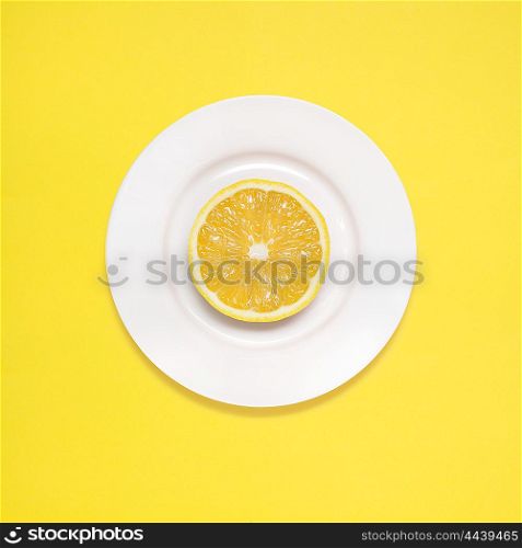 Lemon slice on white plate on yellow background.