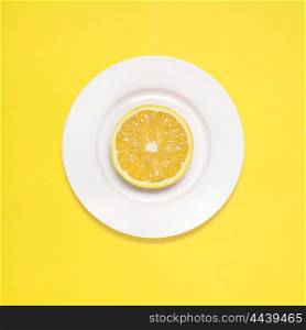 Lemon slice on white plate on yellow background.