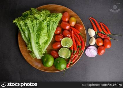 Lemon slice, shallots, garlic, tomatoes, lettuce and peppers on a wooden plate on a black cement floor. Top view.