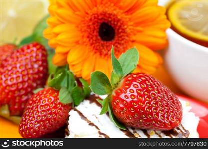 lemon tea,gerbera,cake and strawberries lying on the orange fabric