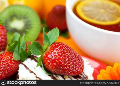 lemon tea, mandarin, kiwi,cake and strawberries lying on the orange fabric