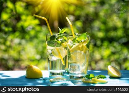 Lemonade and lemons on a blue table against the background of green foliage in the hot summer. Lemonade and lemons on blue table