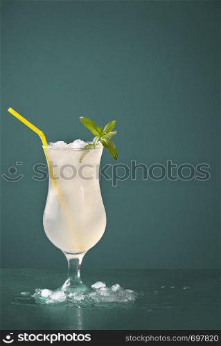 Lemonade drink with ice in a frosty glass on a green table. Summer drink with lemons and peppermint flavors