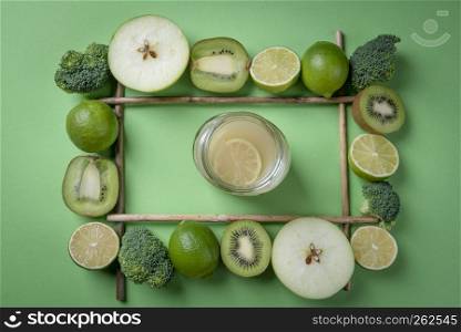 Lemonade in a jar directly above view, surrounded by a frame of green fruits and broccoli. Detoxification food and drink