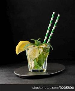 Lemonade in a transparent glass with lemon, lime, rosemary sprigs and mint leaves on a black background