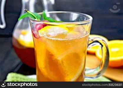 Lemonade in a wineglass and jug with a cherry, lemon and orange, mint on a wooden plank background