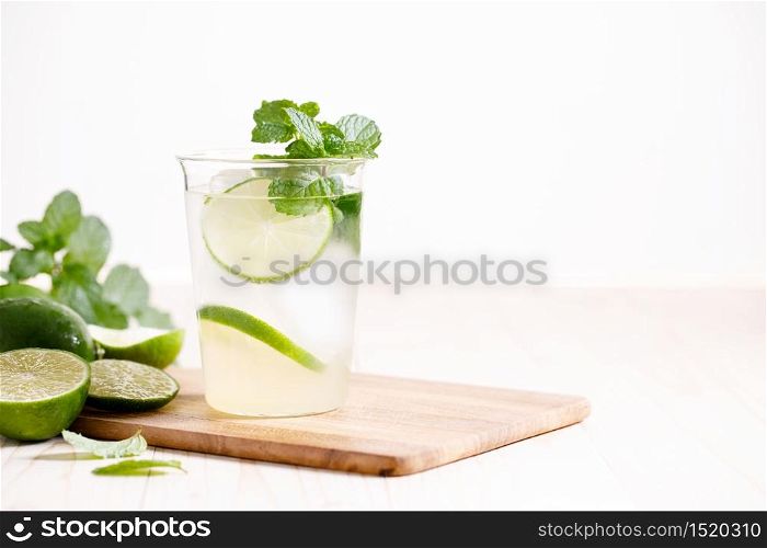 Lemonade or mojito cocktail with fresh lime and mint leaves, cold refreshing drink with ice on wooden table.