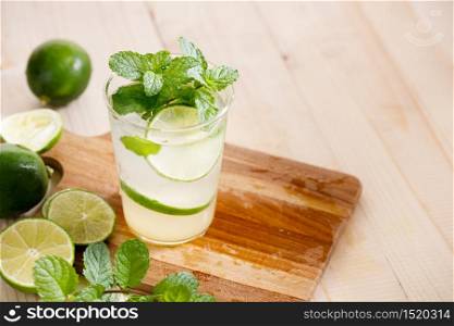 Lemonade or mojito cocktail with fresh lime and mint leaves, cold refreshing drink with ice on wooden table.