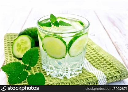 Lemonade with cucumber and mint in a glass on a green napkin on a wooden boards background
