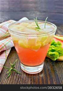 Lemonade with rhubarb and rosemary in a glass, the stems and leaves of rhubarb, a doily on a wooden boards background