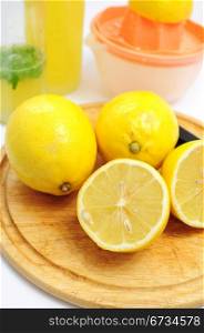 Lemons as ingredients to lemonade, bottles and sqeezer in the background
