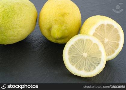Lemons with fresh leaves on black chalkboard from above. Background layout with free text space.