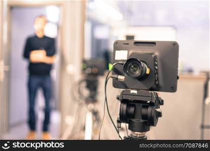 Lens of a film camera in an television broadcasting studio, spotlights and equipment, director in the background