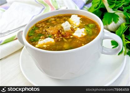 Lentil soup with spinach, tomatoes and feta cheese in a white bowl, napkin, parsley on the background light wooden boards