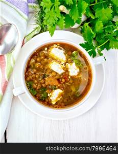 Lentil soup with spinach, tomatoes and feta cheese in a white bowl, spoon on a kitchen towel, parsley on the background light wooden boards on top