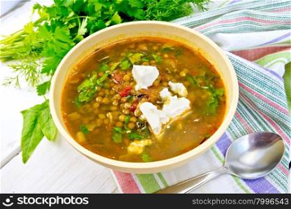 Lentil soup with spinach, tomatoes and feta cheese in a yellow bowl, spoon on a napkin, parsley and spinach on the background light wooden boards
