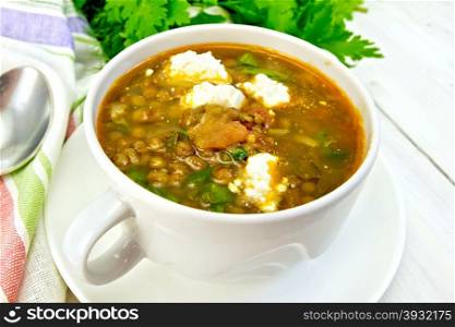 Lentil soup with spinach, tomatoes and feta cheese, napkin, spoon, parsley on a light wooden board