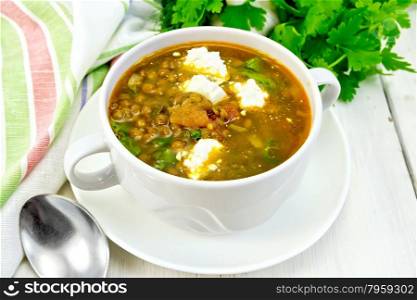Lentil soup with spinach, tomatoes and feta cheese, napkin, spoon, parsley on the background light wooden boards