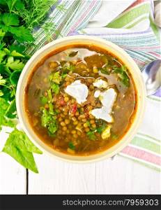 Lentil soup with spinach, tomatoes and feta cheese, spoon on a napkin, parsley on the background light wooden boards on top