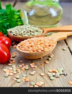Lentils red and green in two wooden spoons, tomatoes, parsley, vegetable oil in a decanter on a wooden boards background
