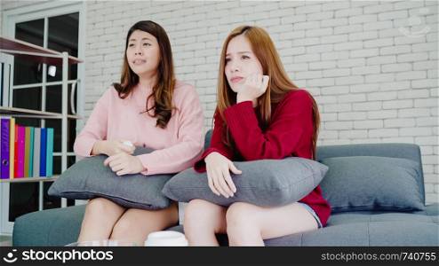 Lesbian Asian couple crying while watching drama in TV in living room at home, sweet couple enjoy romantic moment while lying on the sofa when relaxed at home. Lifestyle couple relax at home concept.