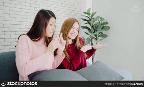 Lesbian Asian couple sing a song and dancing in living room at home, sweet couple enjoy funny moment while lying on the sofa when relax at home. Lifestyle couple relax at home concept.