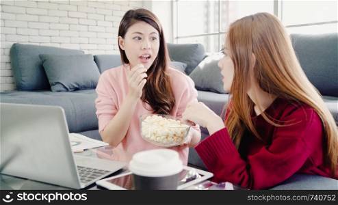 Lesbian Asian couple using laptop making budget in living room at home, sweet couple enjoy love moment while lying on the sofa when relaxed at home. Lifestyle couple relax at home concept.