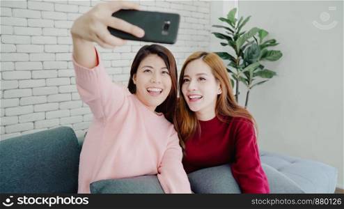 Lesbian Asian couple using smartphone selfie in living room at home, sweet couple enjoy funny moment while lying on the sofa when relaxed at home. Lifestyle couple relax at home concept.