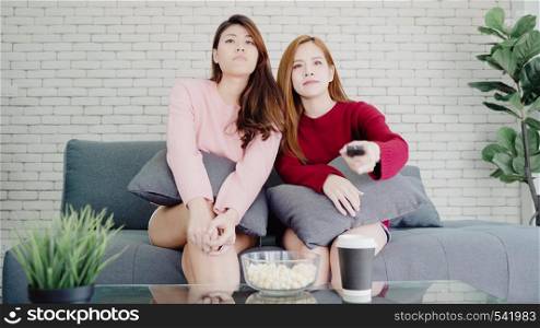 Lesbian Asian couple watching TV laugh and eating popcorn in living room at home, sweet couple enjoy funny moment while lying on the sofa when relaxed at home. Lifestyle couple relax at home concept.