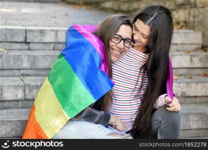 Lesbian couple sitting on steps hugging with rainbow flag at urban scenery. High quality 4k footage. Lesbian couple sitting on steps hugging with rainbow flag at urban scenery.