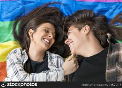 Lesbian couple wearing a lgbt rainbow flag lying on the floor. Affectionate moment between two women under a lgbt flag. High quality photo.. Lesbian couple wearing a lgbt rainbow flag lying on the floor. Affectionate moment between two women under a lgbt flag.