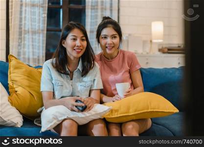 Lesbian lgbt women couple watching television at home, Asian female lover feeling happy funny moment looking drama entertainment together on sofa in living room in night concept.