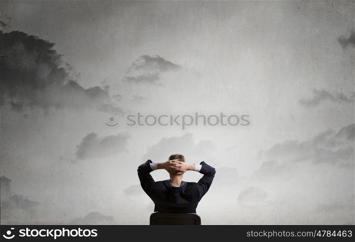 Let me think it over. Rear view of businessman sitting on chair with hands on head