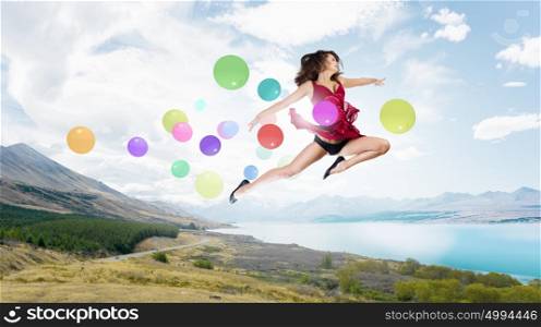 Let&rsquo;s celebrate. Young cheerful lady in red dress jumping high