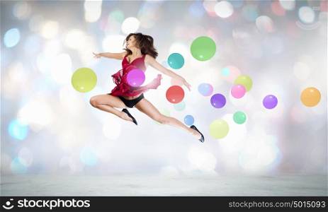 Let&rsquo;s celebrate. Young cheerful lady in red dress jumping high