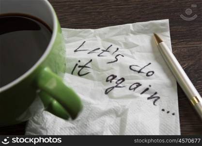 Lets do it again. Romantic message written on napkin and coffee cup on wooden table