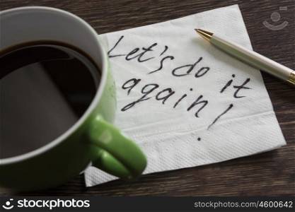Lets do it again. Romantic message written on napkin and coffee cup on wooden table