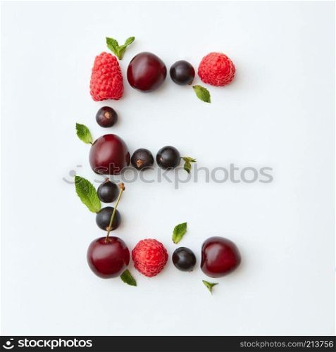 Letter E english alphabet in the form of a pattern of natural organic berries - ripe fresh raspberry, black currant, cherry, green mint leaf isolated on a white background. Top view.. Fresh fruits pattern of letter E english alphabet from natural ripe berries - black currant, cherries, raspberry, mint leaf isolated on a white background. Top view.