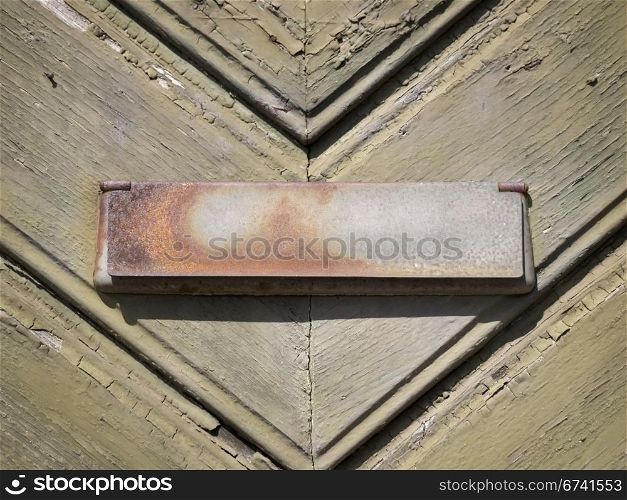 Letter flap triangle. rusty letter flap on olive-green door