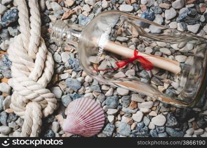 Letter in bottle lying on seashore with marine rope and seashells