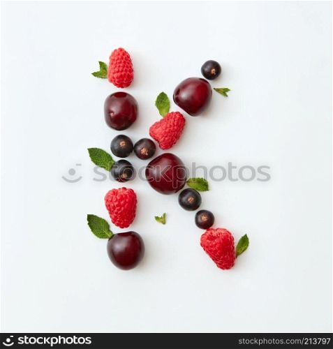 Letter K english alphabet in the form of a pattern of natural organic berries - ripe fresh raspberry, black currant, cherry, green mint leaf isolated on a white background. Flat lay. Summer pattern of letter K english alphabet from natural ripe berries - black currant, cherries, raspberry, mint leaf isolated on a white background.